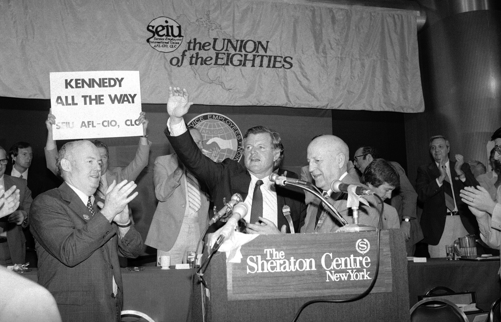 John Sweeney, left, was the incoming president of the Service Employees International Union in June 1980 when Senator Edward M. Kennedy (waving) spoke to its convention in New York. Mr. Kennedy was seeking the Democratic presidential nomination. At right in the foreground was the outgoing union president, George Hardy. Credit: Associated Press